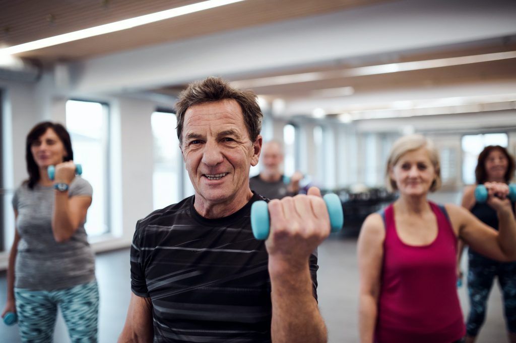 Group of cheerful seniors in gym doing exercise with dumbbells.